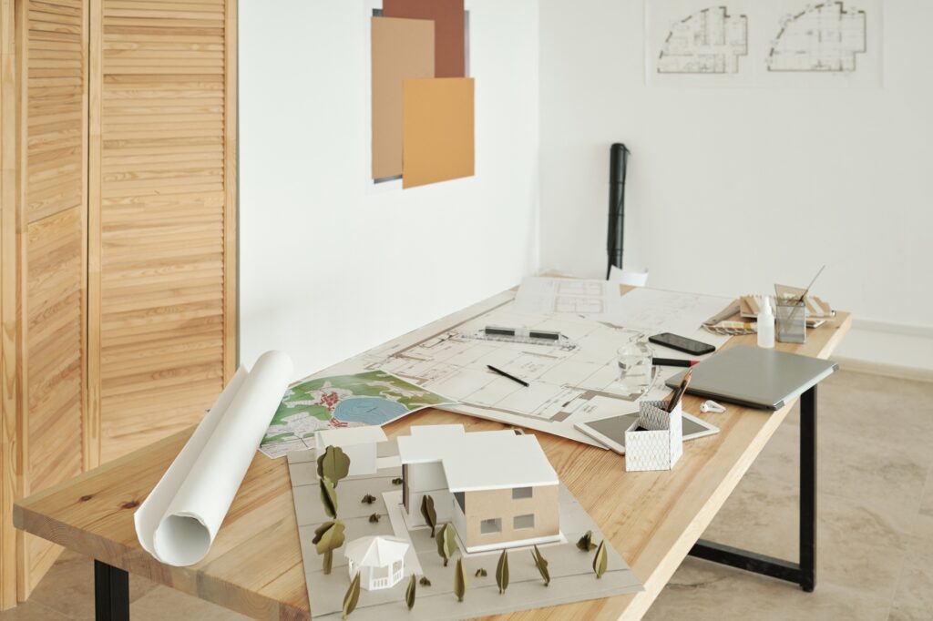 Wooden table with paper house models, sketches and mobile gadgets